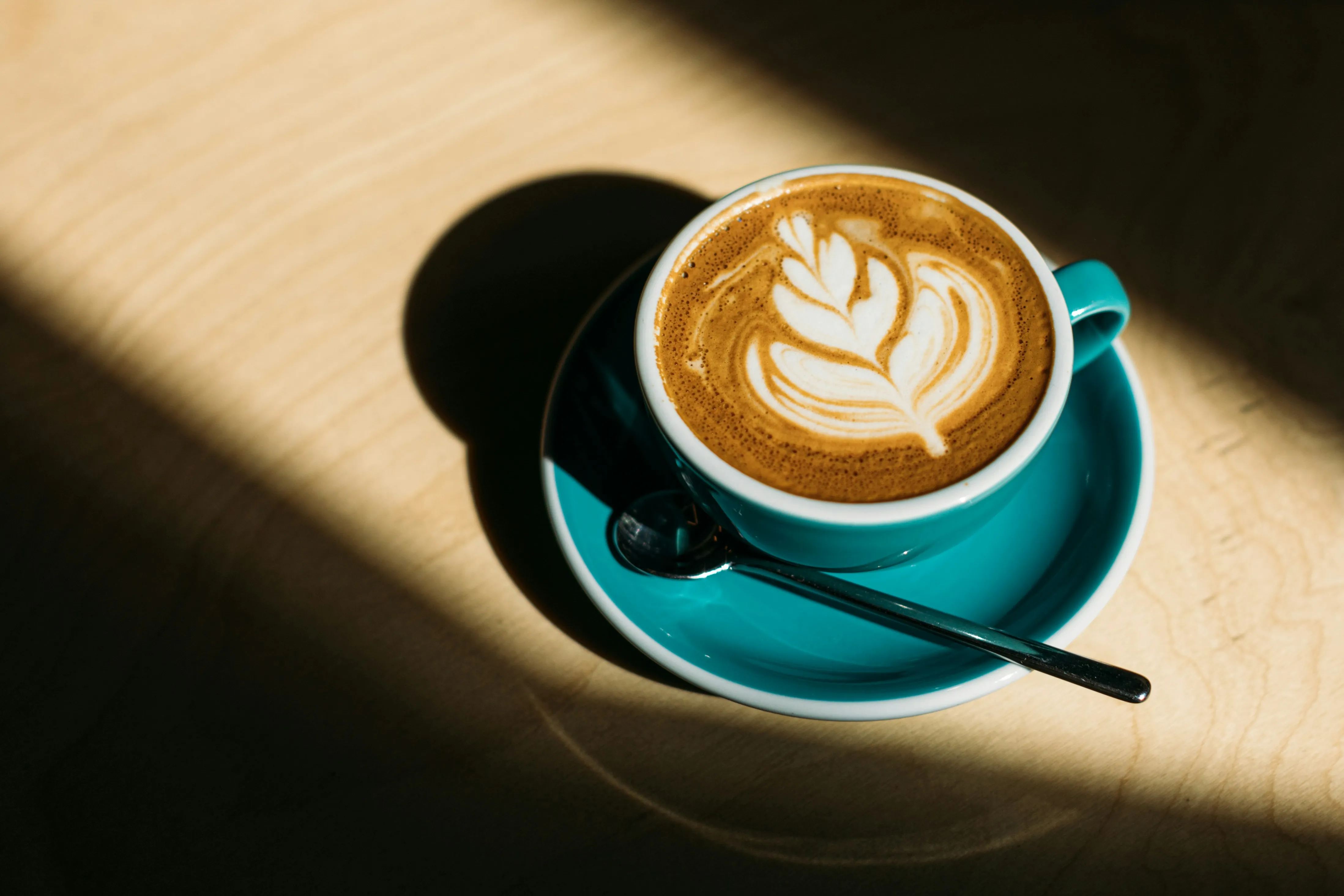 Latte with foam art in a teal cup and saucer
