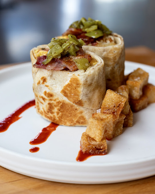 Breakfast burrito plated with red chile and crispy potatoes